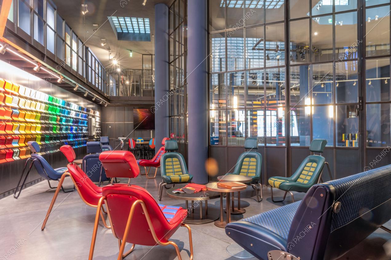 Poltrone colorate di design e tavolini che si affacciano, tramite le vetrate in stile industriale, sulla stanza dalle pareti blu