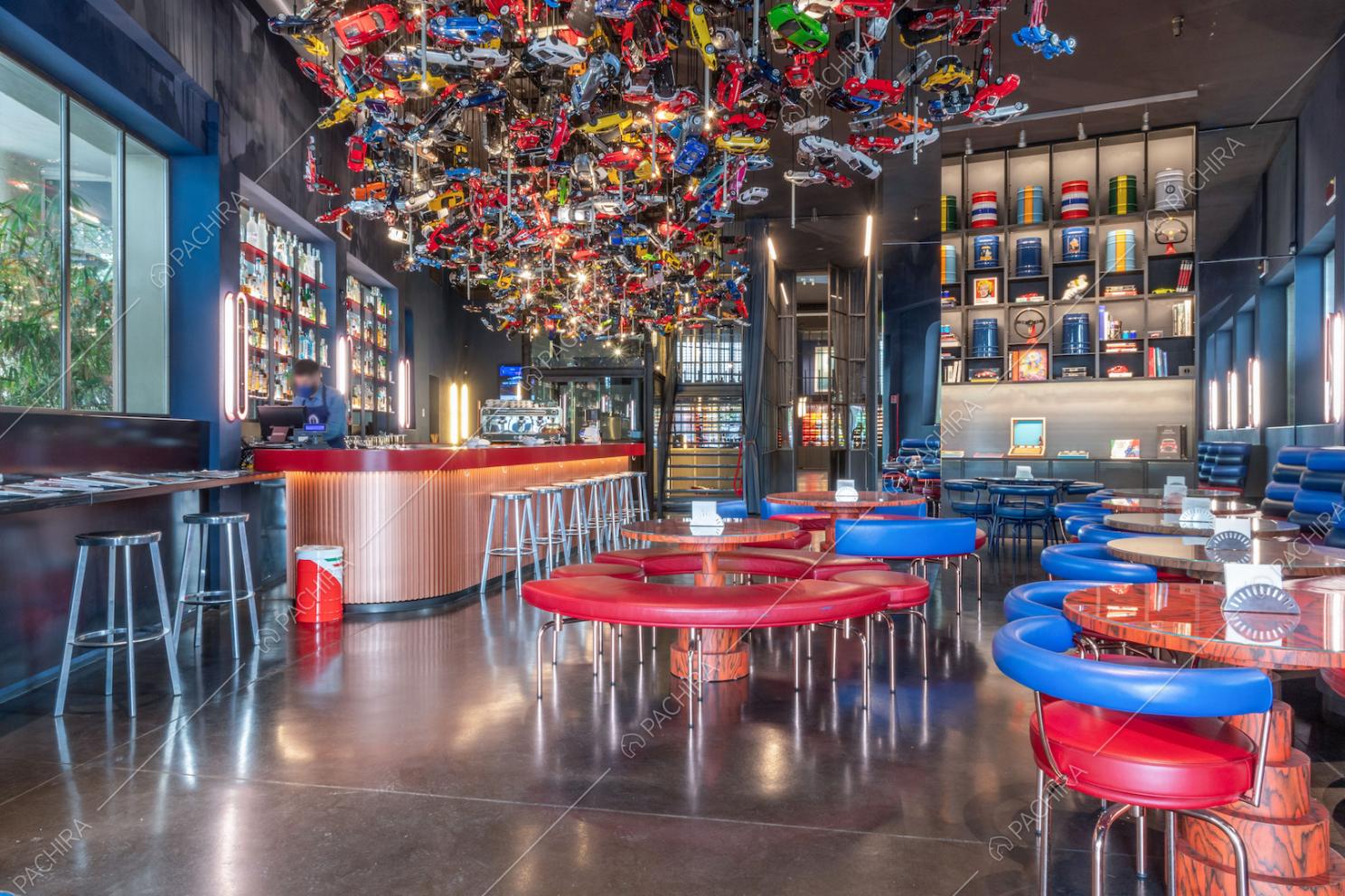 Sala con grande lampadario ricavato da automobili giocattolo, bancone rosso con sgabelli e divanetti rossi e blu ai tavoli