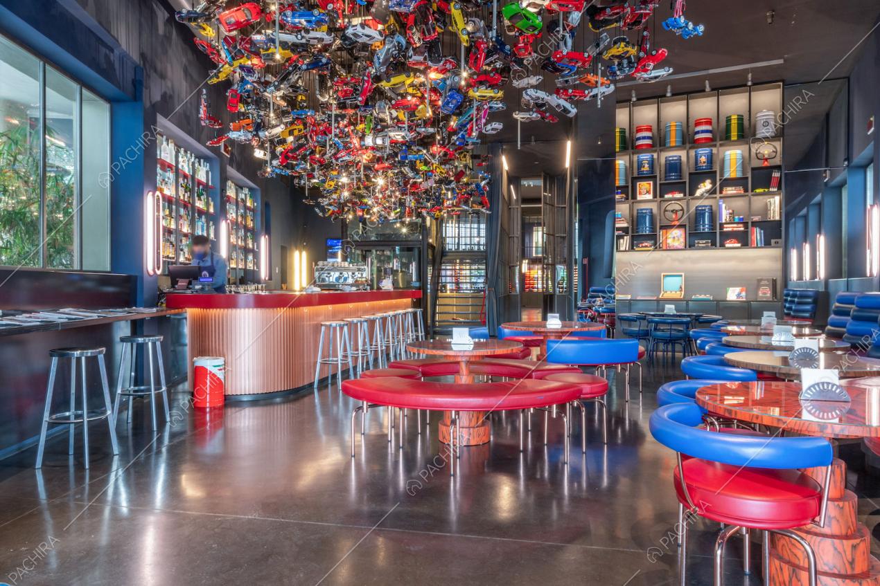 Sala con grande lampadario ricavato da automobili giocattolo, bancone rosso con sgabelli e divanetti rossi e blu ai tavoli