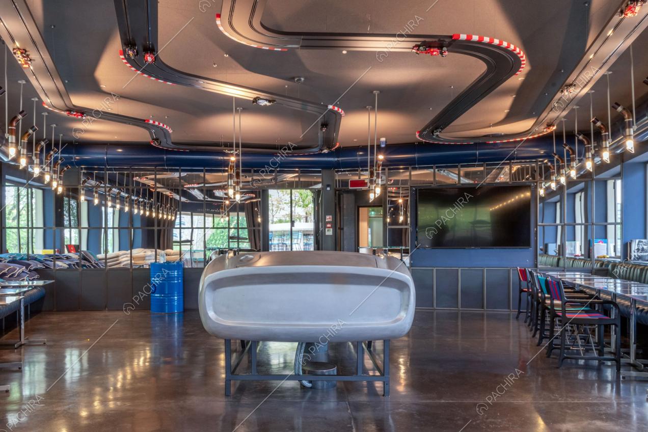 Grande sala con pista per macchinine sul soffitto, vetrate in stile industriale e tavolini