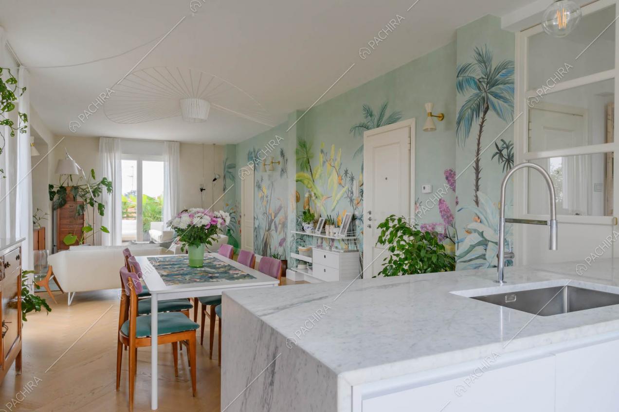 Dalla penisola della cucina con piano da lavoro in marmo vista sul salotto con carta da parati a fantasia tropicale