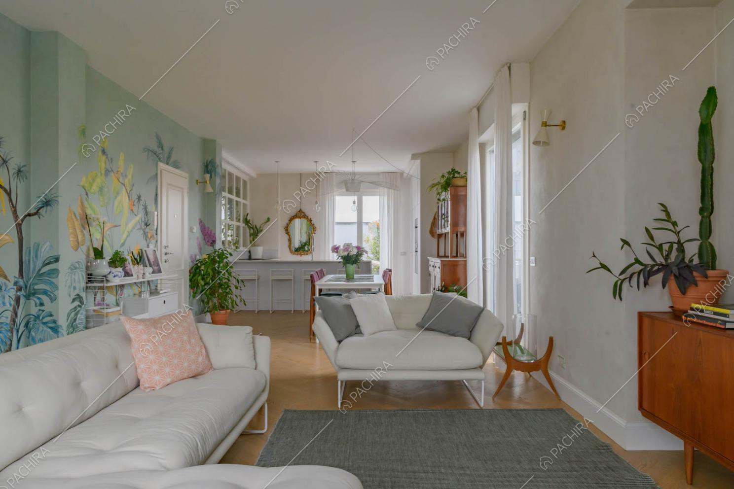 Sala con divani bianchi, pavimento in parquet e carta da parati a fantasia tropicale