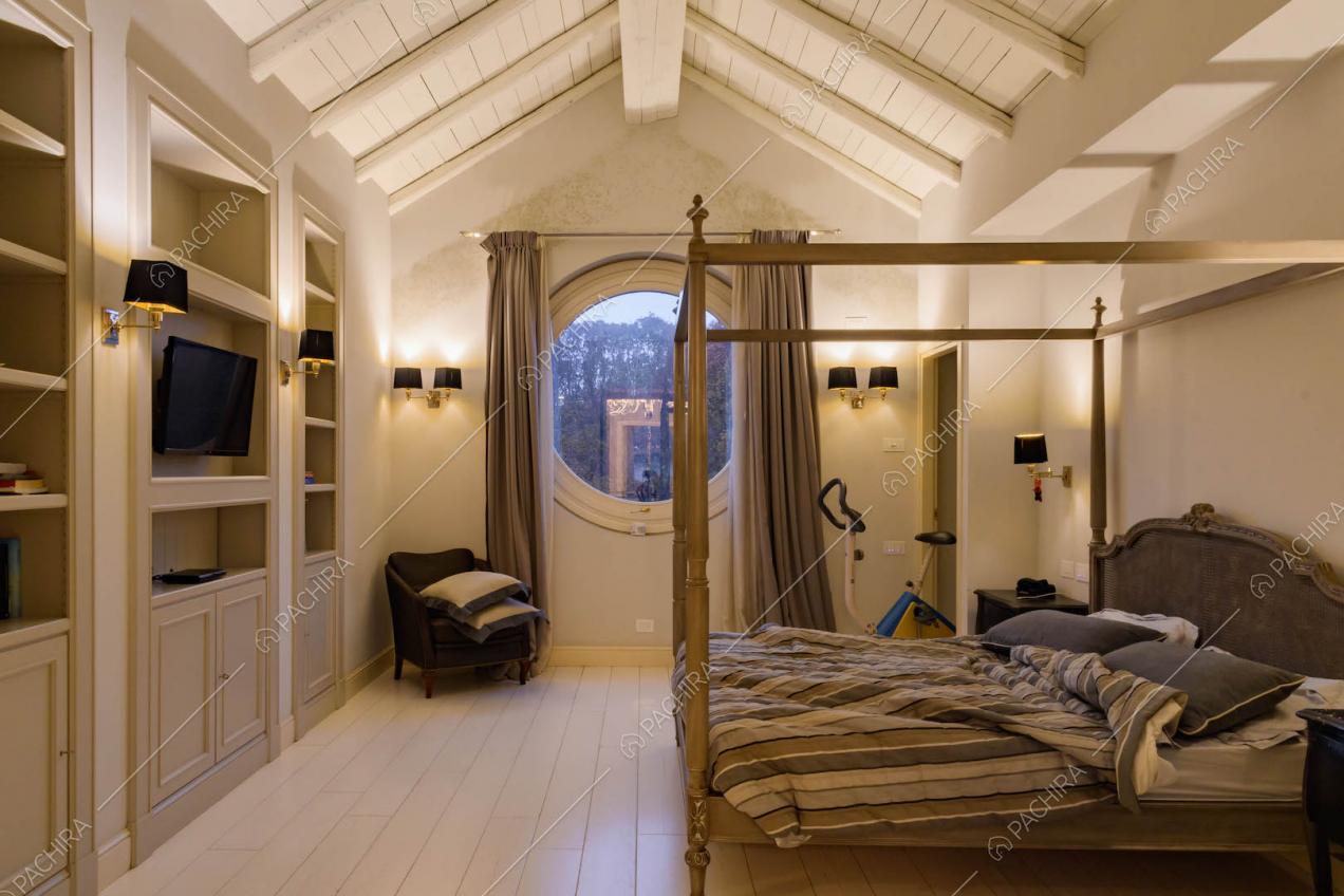 Letto matrimoniale a baldacchino nella camera con parquet bianco e finestra a oblò