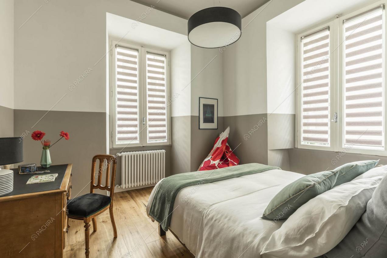 Luminosa camera da letto matrimoniale con pavimento in parquet e pareti bianche e grigie