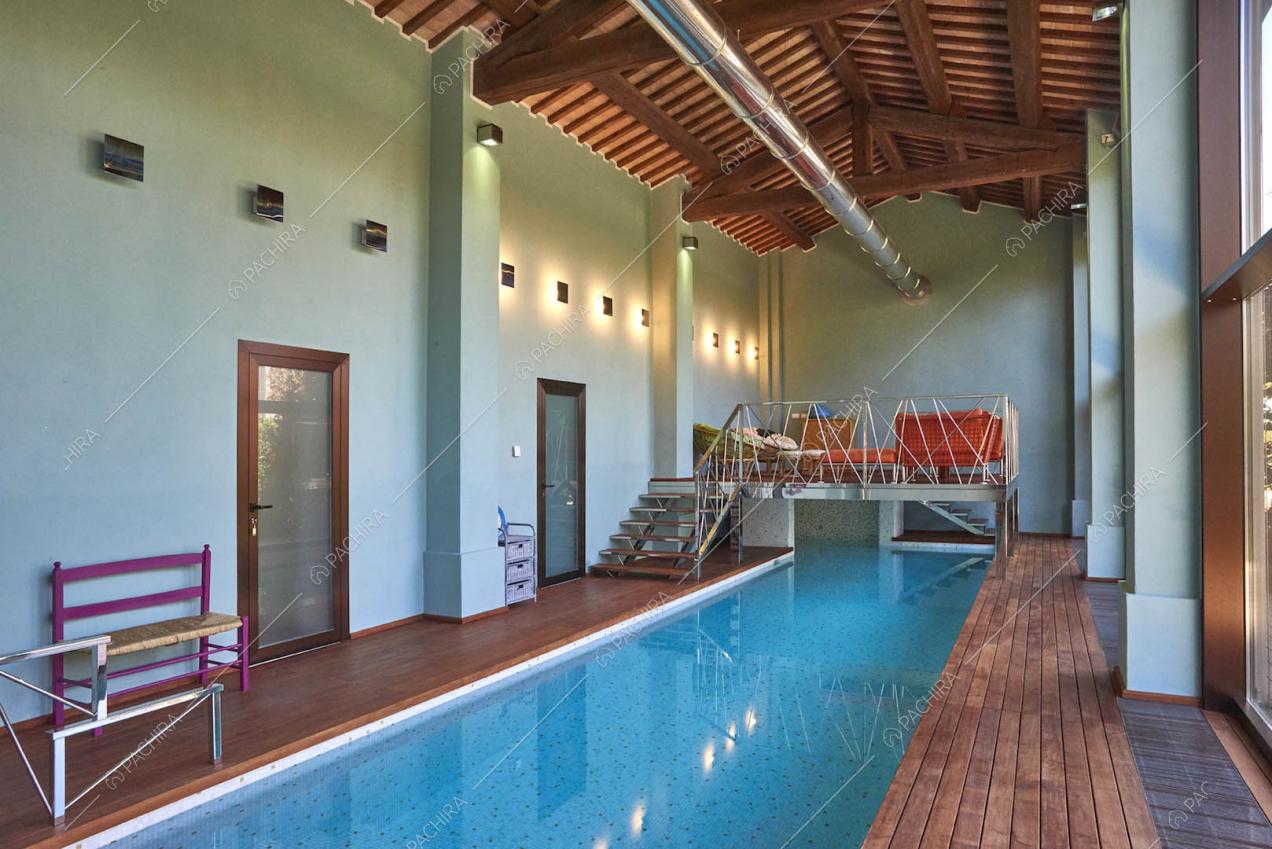 Piscina interna nella luminosa sala con soppalco, pavimento in parquet e soffitto in travi in legno
