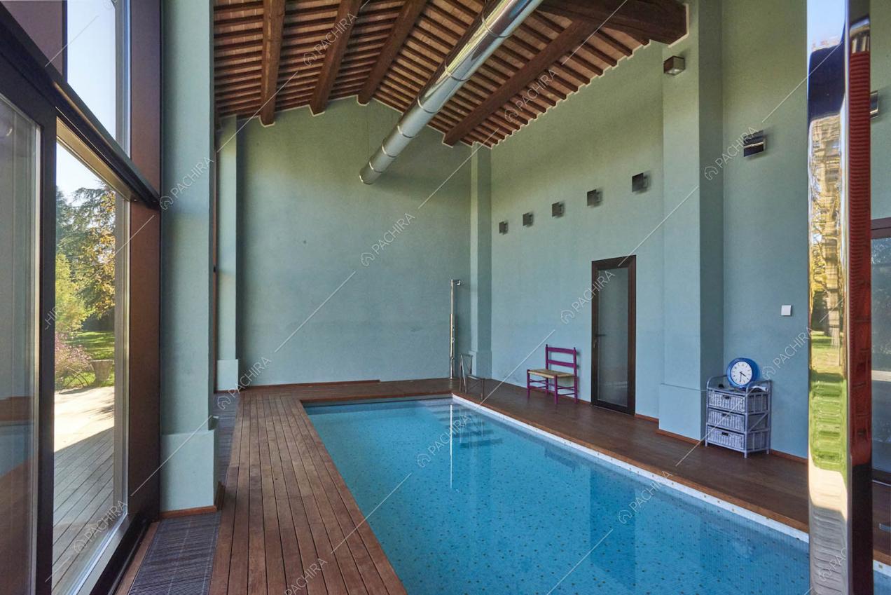 Luminosa piscina interna con pavimento in parquet e soffitto in travi in legno a vista