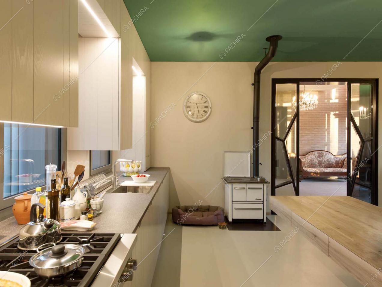 Grande cucina con fornelli a gas, pavimento bianco, soffitto verde e vista sul salotto