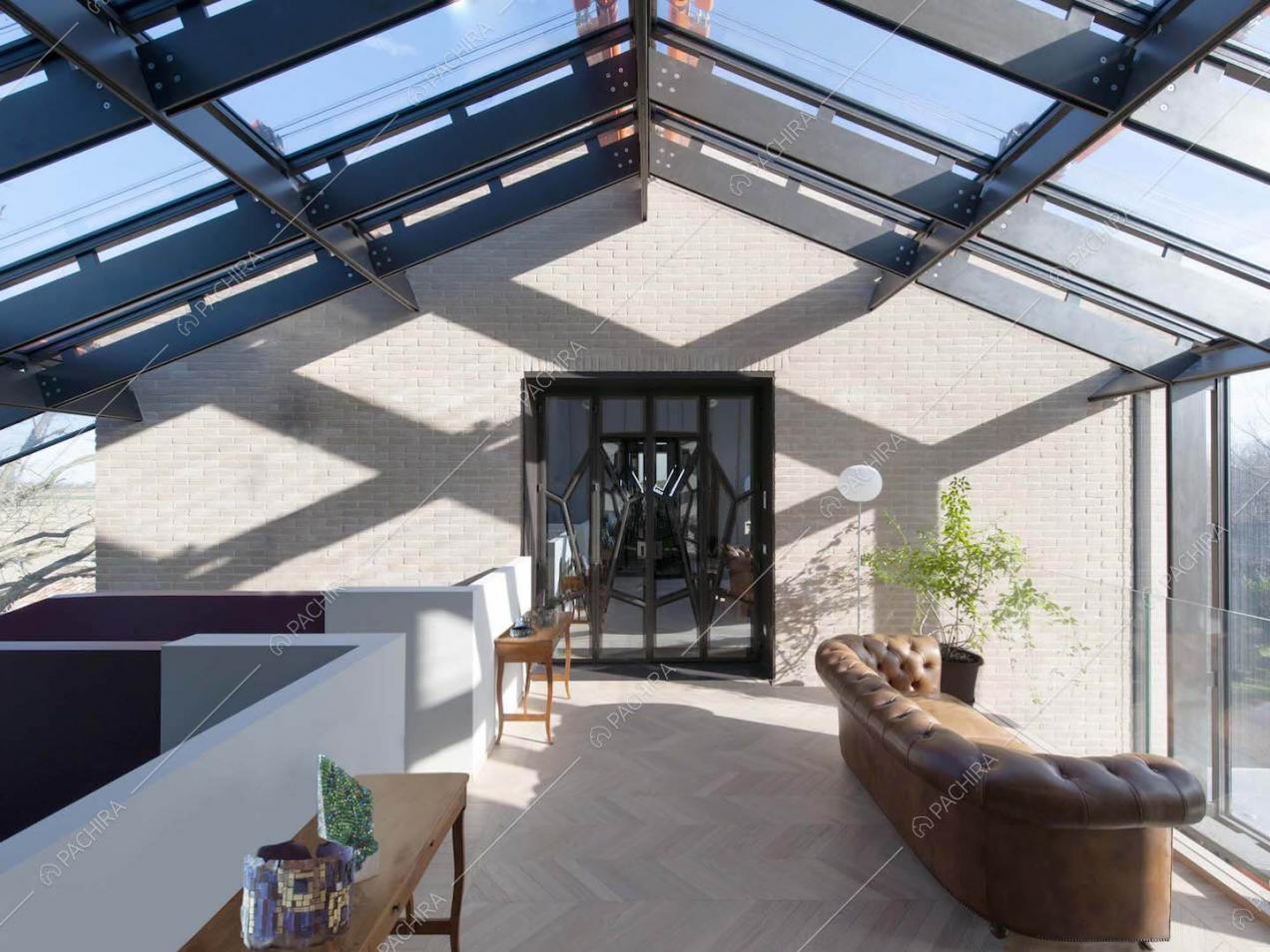 Soffitta con parete in mattoncini a vista, pavimento in parquet e vetrate su pareti e soffitto