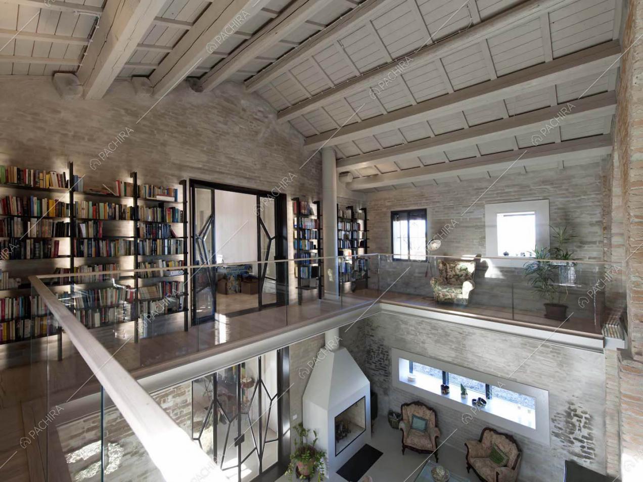 Soppalco con balaustra in vetro, libreria, soffitto intravi in legno a vista e camino