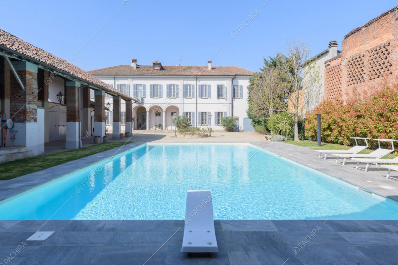 Grande piscina con trampolino e vista sulla struttura principale dagli esterni bianchi
