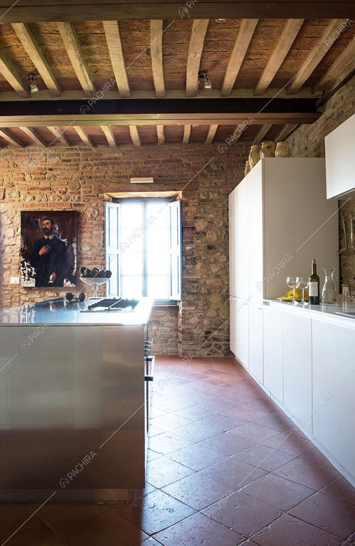 Cucina a isola in acciaio con fornelli a gas e soffitto in travi in legno a vista