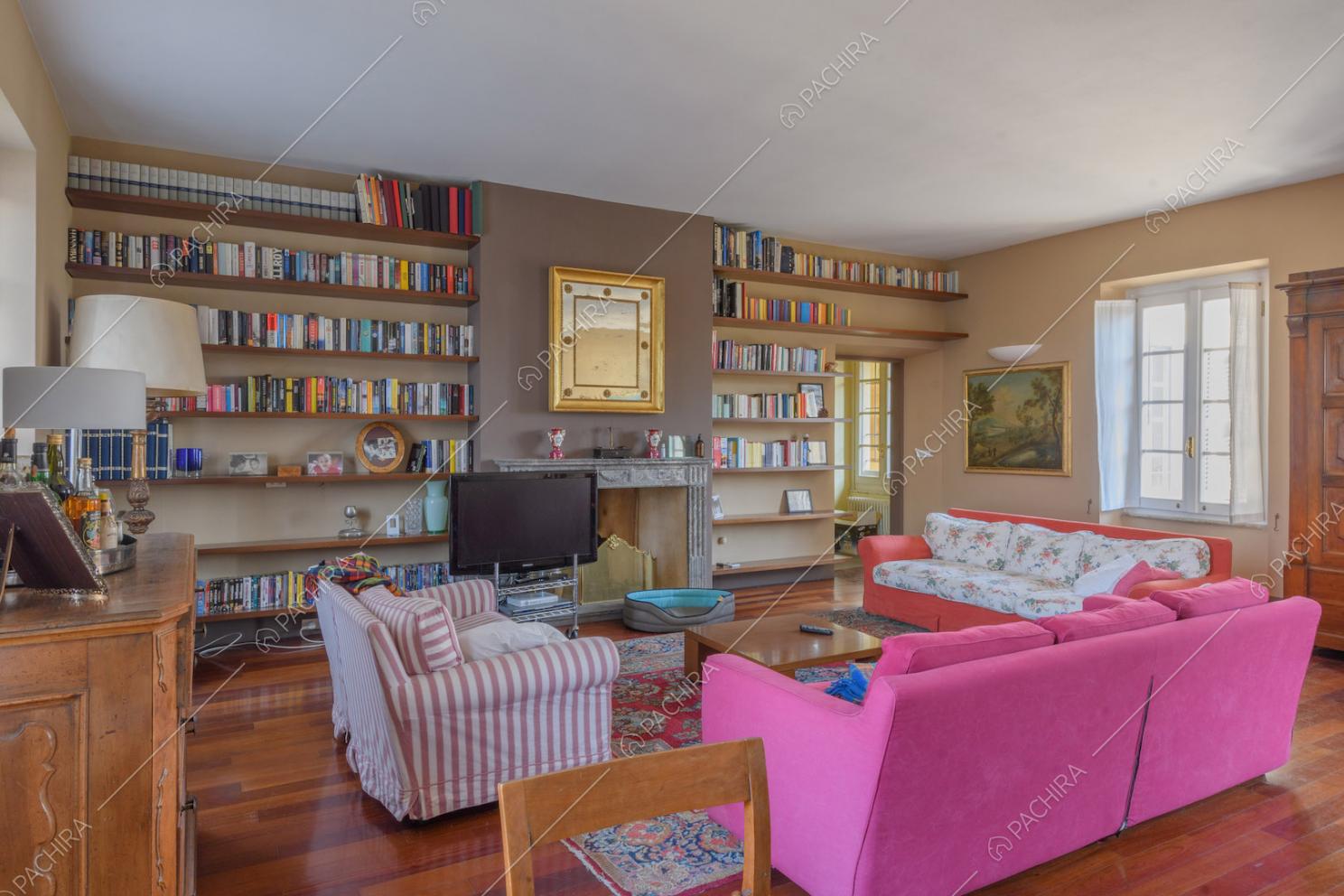 Luminosa zona living con pavimento in parquet, libreria e camino con cornice in marmo