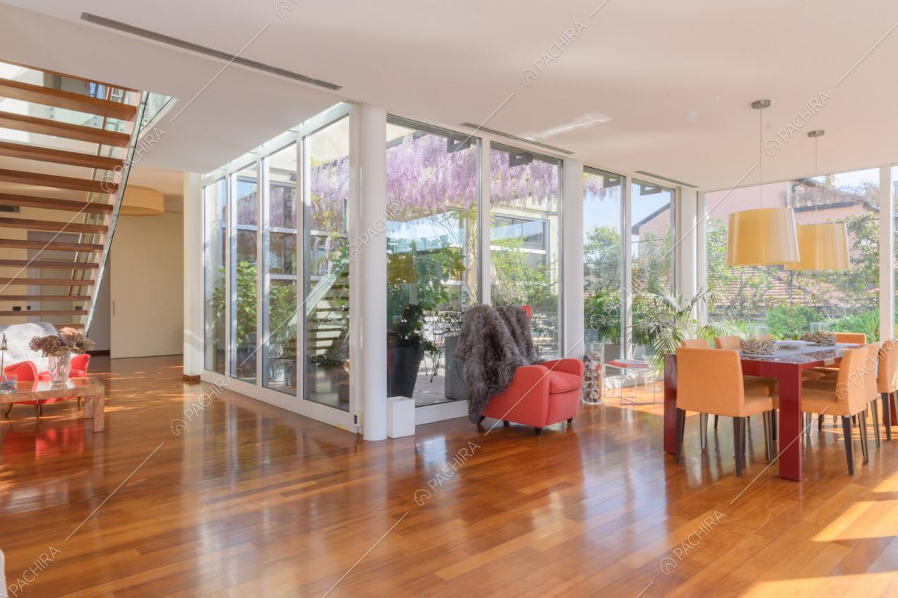 Zona living con vetrate, tavolo da pranzo rosso, scale e pavimento in parquet