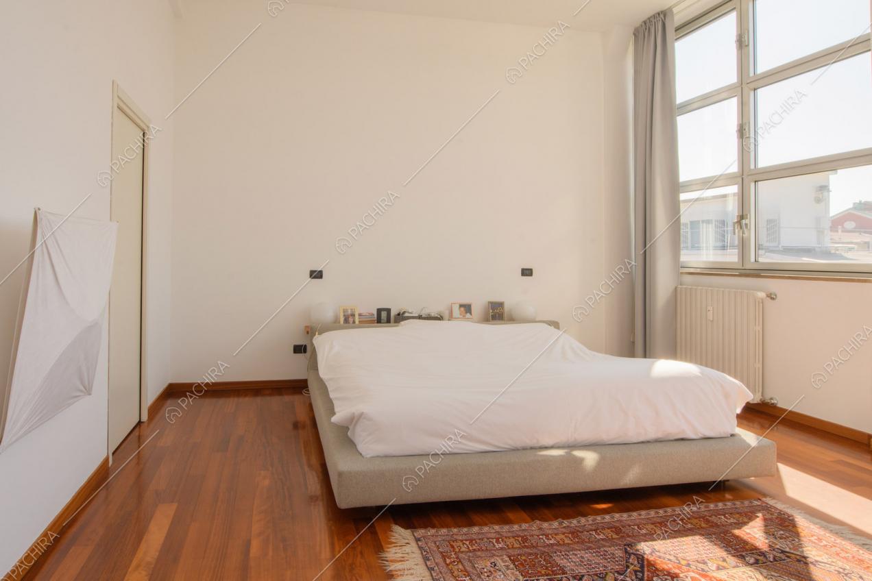 Camera da letto matrimoniale dalle pareti bianche con pavimento in parquet e vetrate