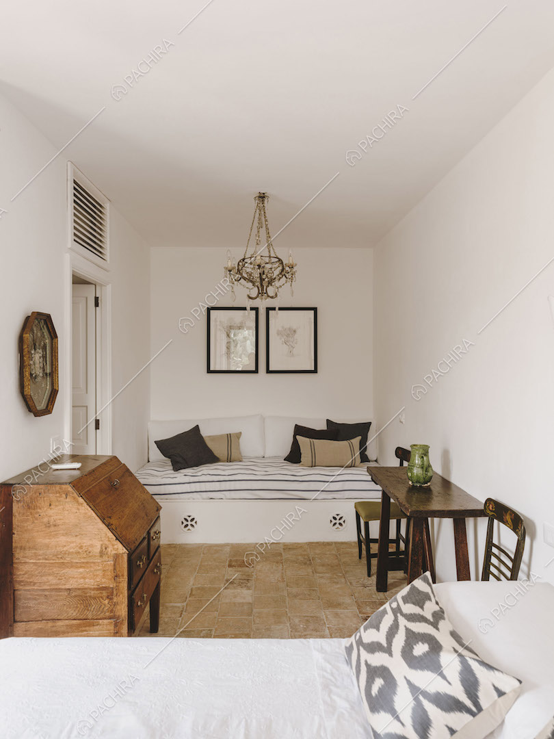 Letto singolo nella camera con pareti bianche e lampadario antico