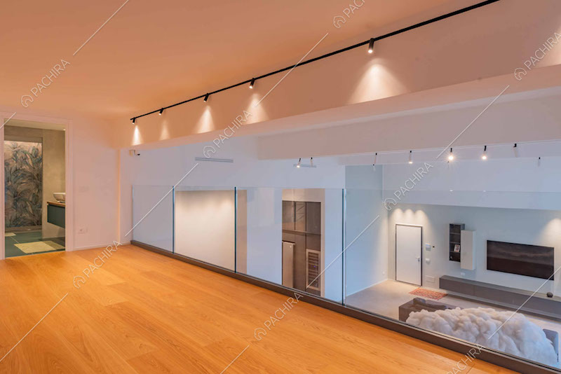 Balconata con pavimento in parquet, parapetto in vetro e vista sul grande salone