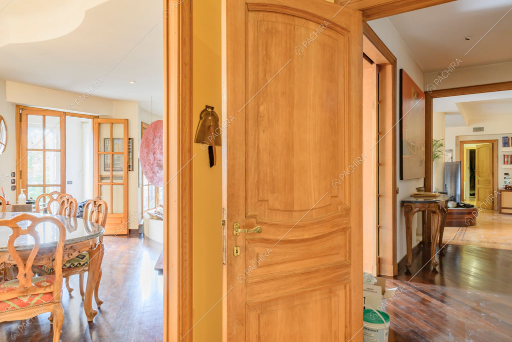 Porta con boiserie, scorcio sulla sala con tavolo da pranzo e sul corridoio