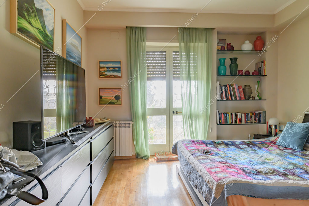 Camera da letto matrimoniale con pavimento in parquet, porte-finestre e tende verdi