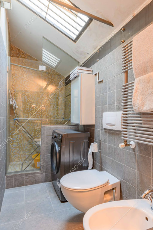 Bagno con pavimento e pareti in piastrelle grigie, box doccia e lucernario
