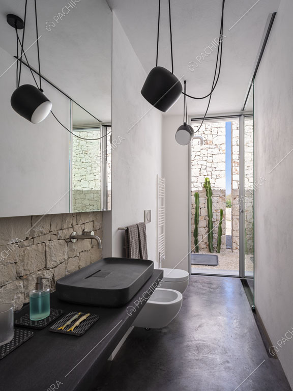 Pareti bianche, faretti e pavimento nero nel luminoso bagno con sanitari sospesi