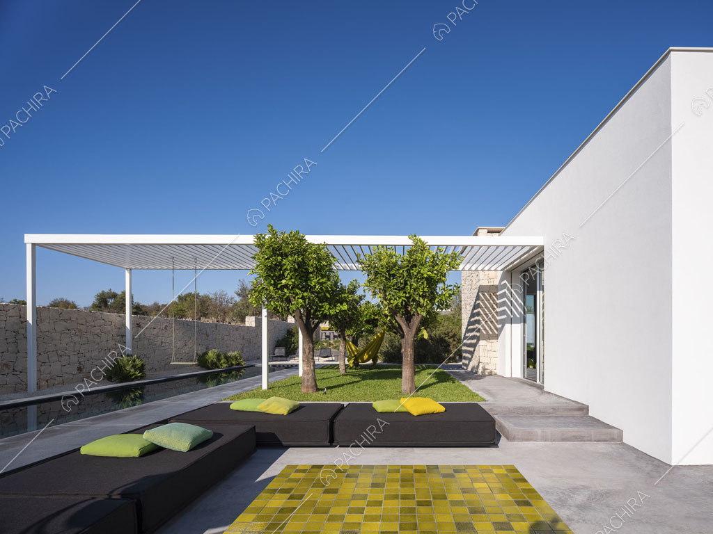 Giardino con pouf neri, piante, piscina e patio bianco