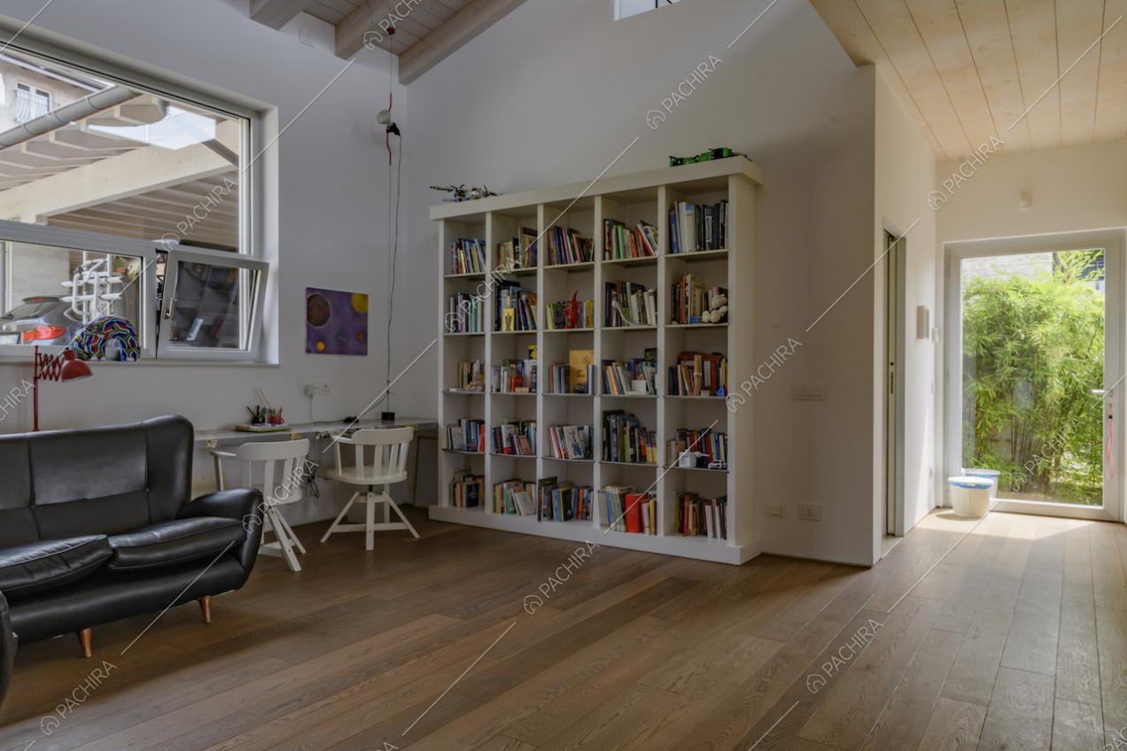 Divano nero in pelle, scrivania con sedie bianche e libreria nel salotto con pavimento in parquet