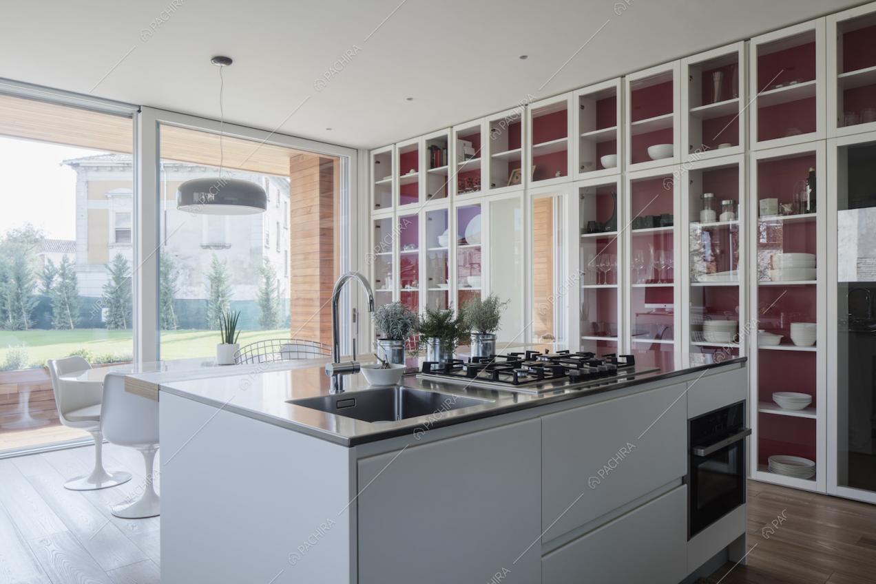 Isola bianca con lavandino e fornelli a gas nella cucina con la credenza a tutta parete in vetro