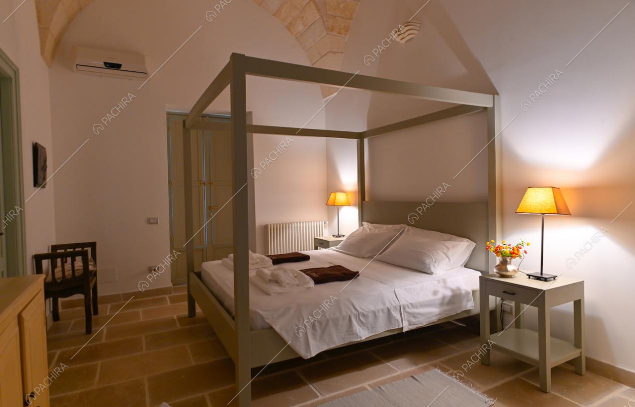 Camera matrimoniale con letto a baldacchino, pareti bianche e pavimento in pietra