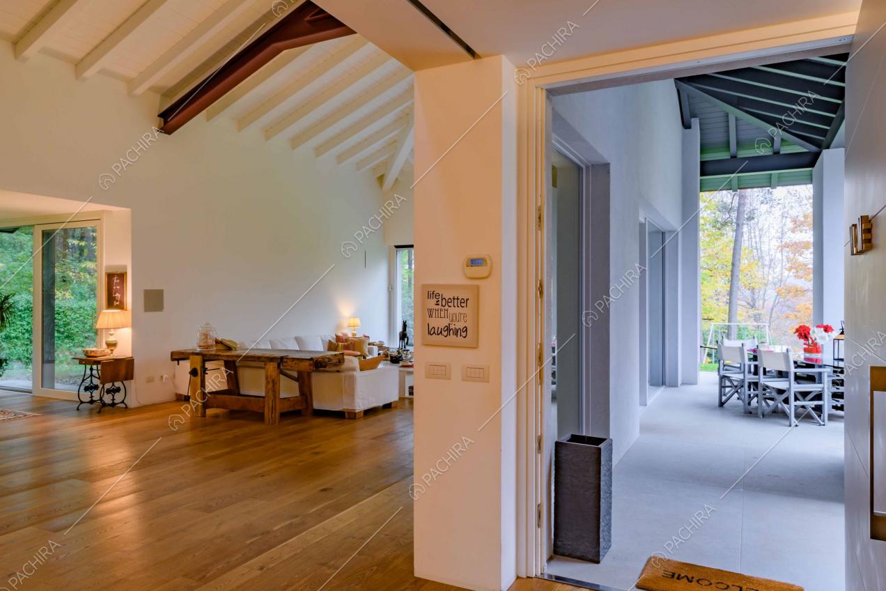 Vista sul salotto con pavimento in parquet e sulla veranda total white con soffitto in travi in legno a vista