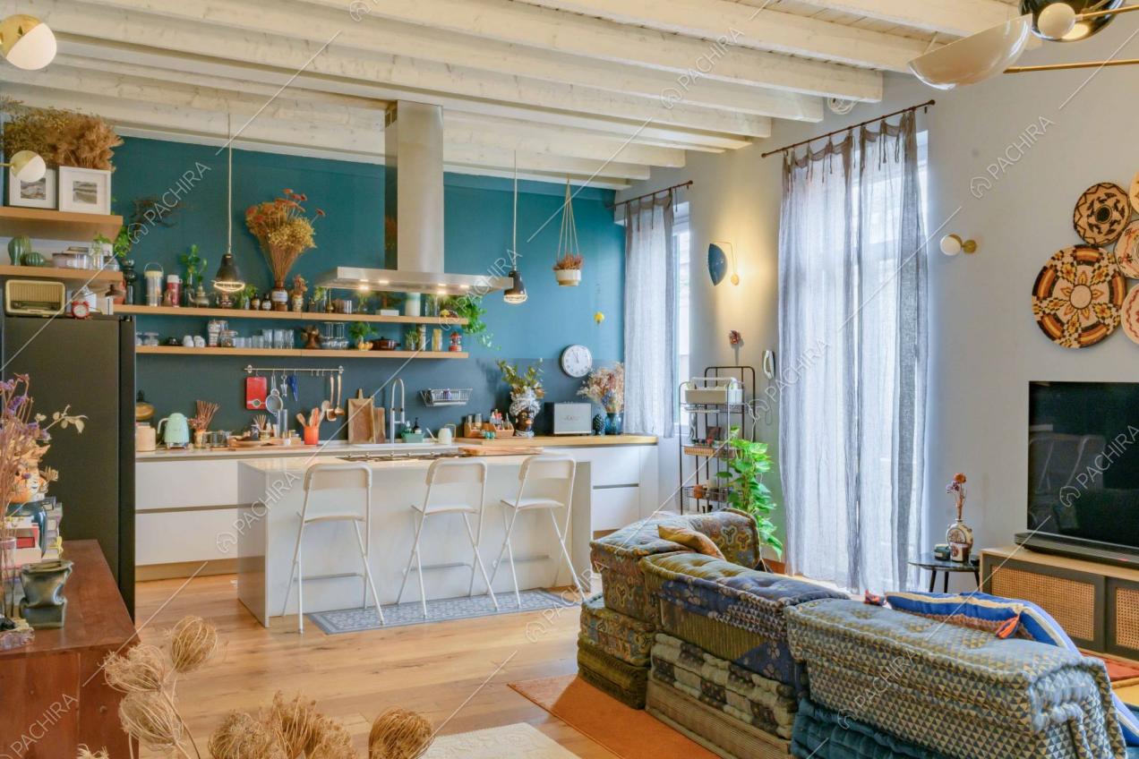 Luminosa sala con cucina a vista, parete blu e soffitto bianco in travi in legno a vista