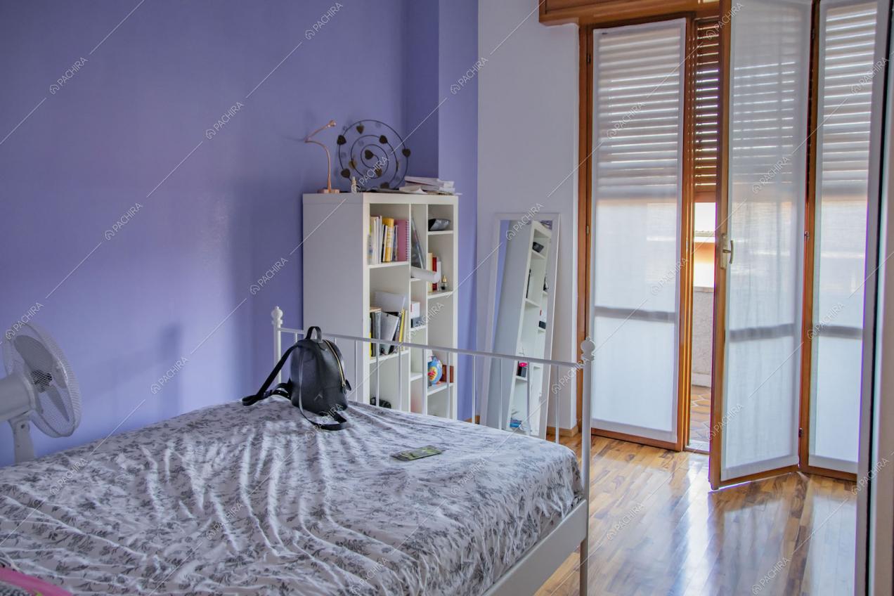 Camera da letto con parete lilla, pavimento in parquet e porta-finestra