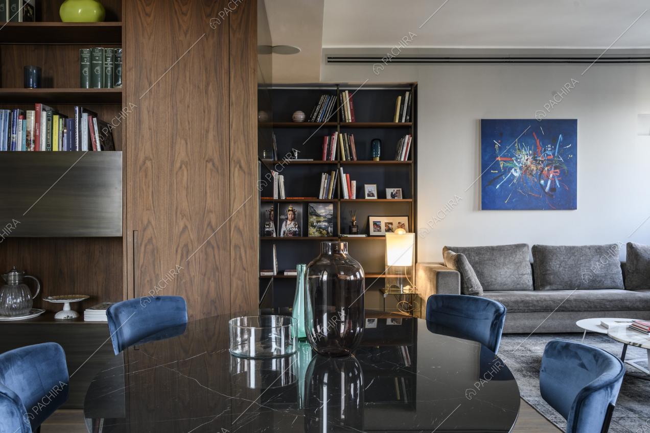 Tavolo da pranzo tondo con sedie in velluto blu circondato da librerie