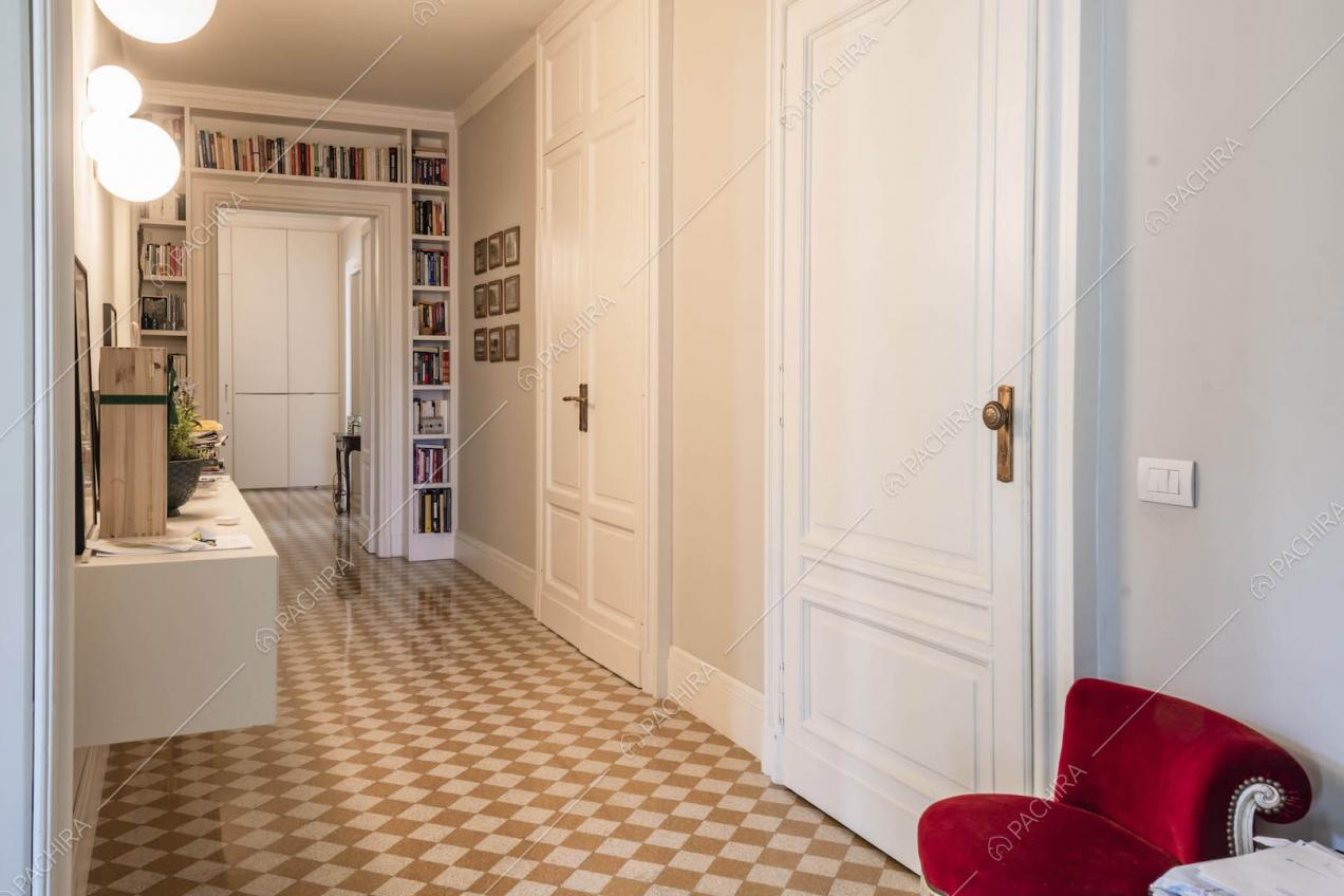 Porte bianche con boiserie nel lungo corridoio con pavimento a scacchi e poltrone in velluto rosso