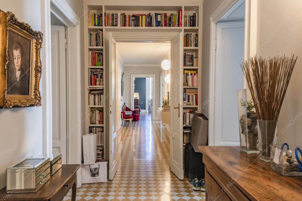Libreria bianca incornicia la porta del lungo corridoio con pavimento a scacchi