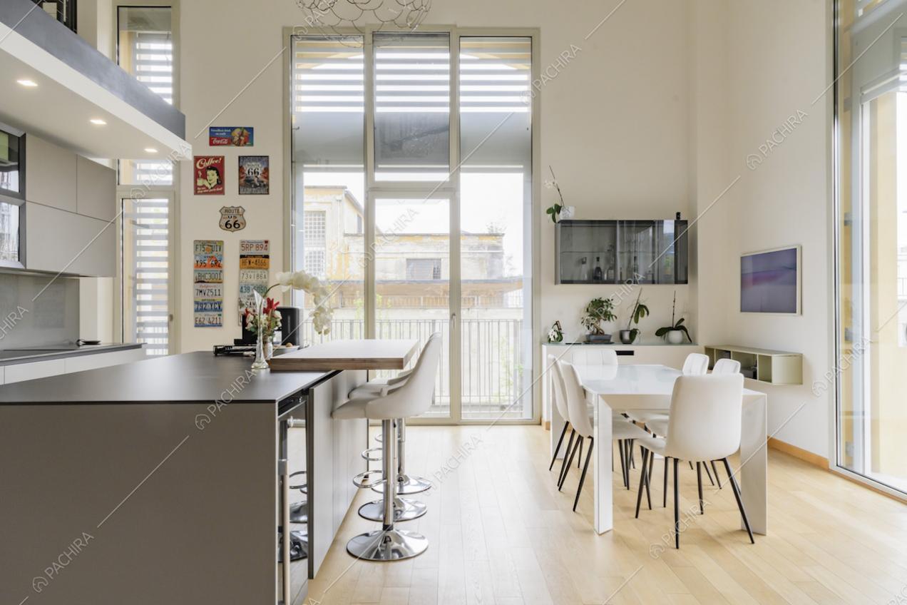 Isola e tavolo da pranzo bianco nella cucina illuminata dalle porte-finestre con vista sul giardino