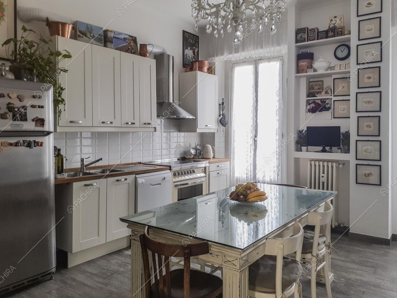 Cucina con mobili bianchi e quadretti appesi alla parete