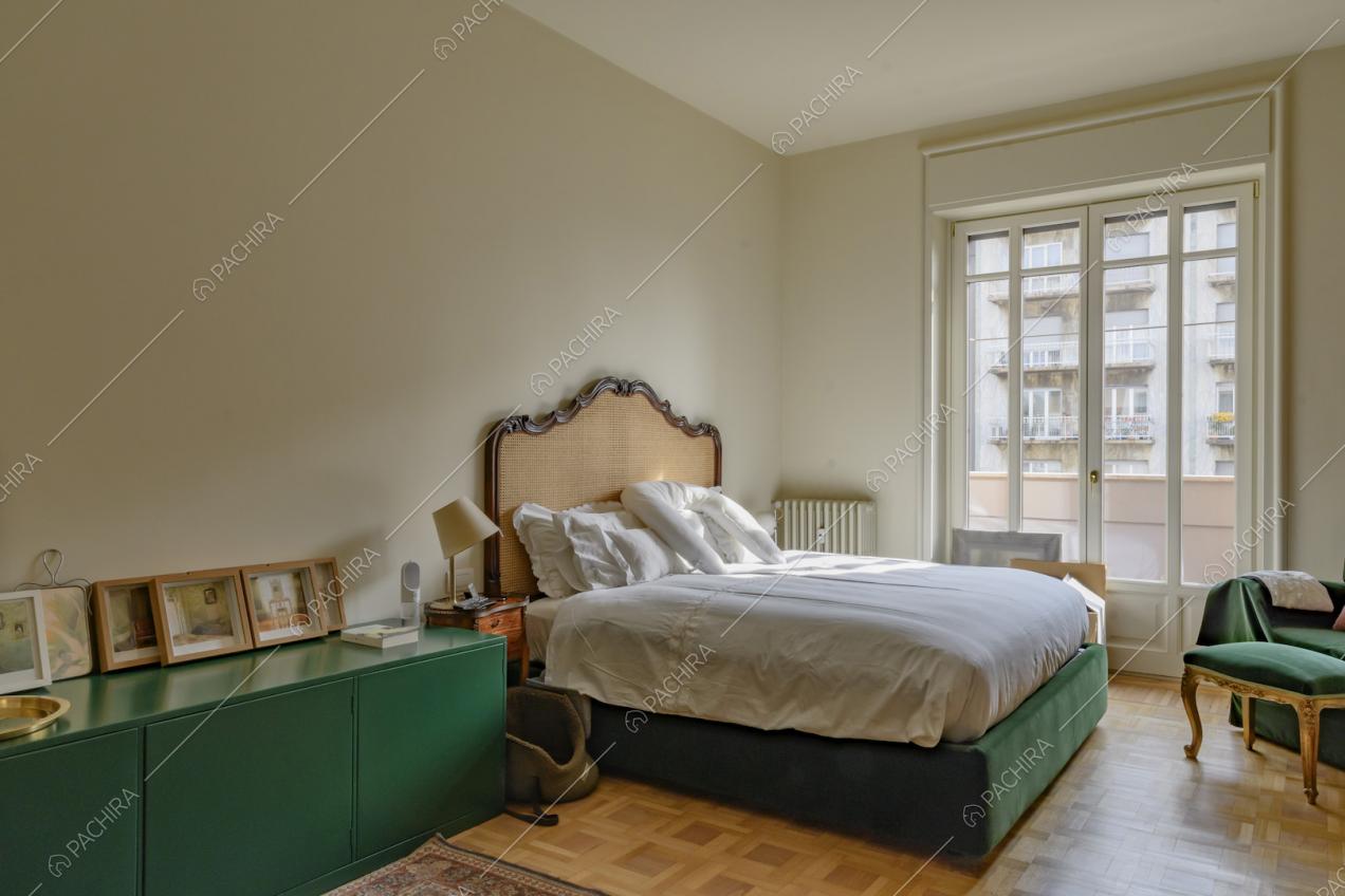 Camera da letto matrimoniale dalle pareti beige, armadietto verde e porta-finestra
