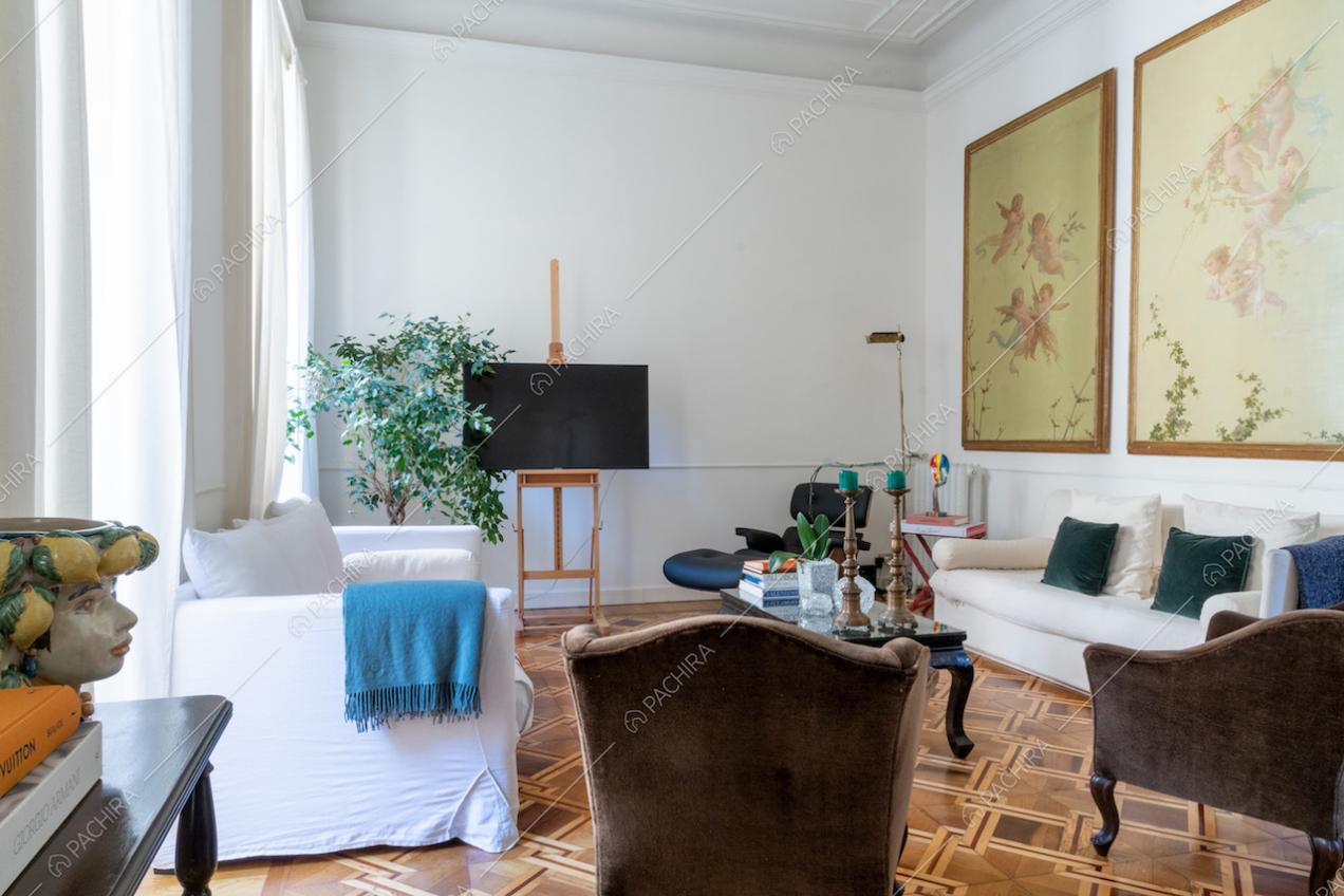 Salotto con pavimento in parquet, pareti bianche con boiserie e ampie vetrate che lo illuminano