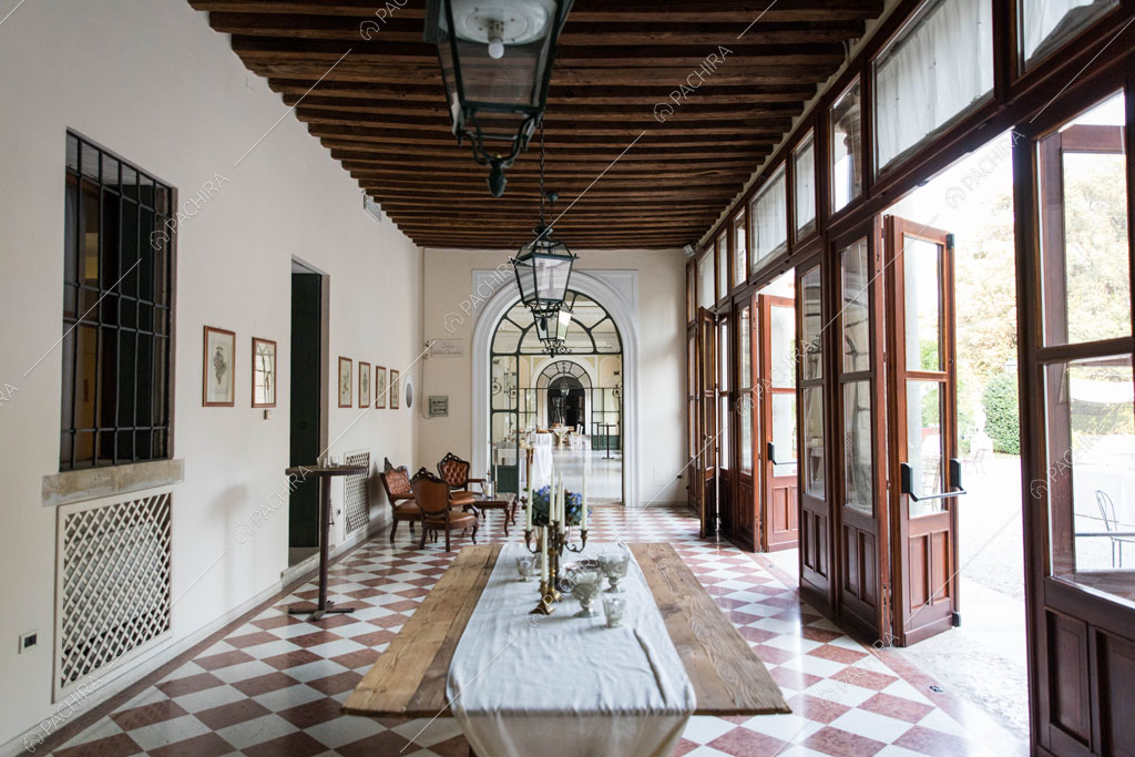 Pavimento a scacchi marrone e bianco nel corridoio con travi a vista sul soffitto e porte-finestre