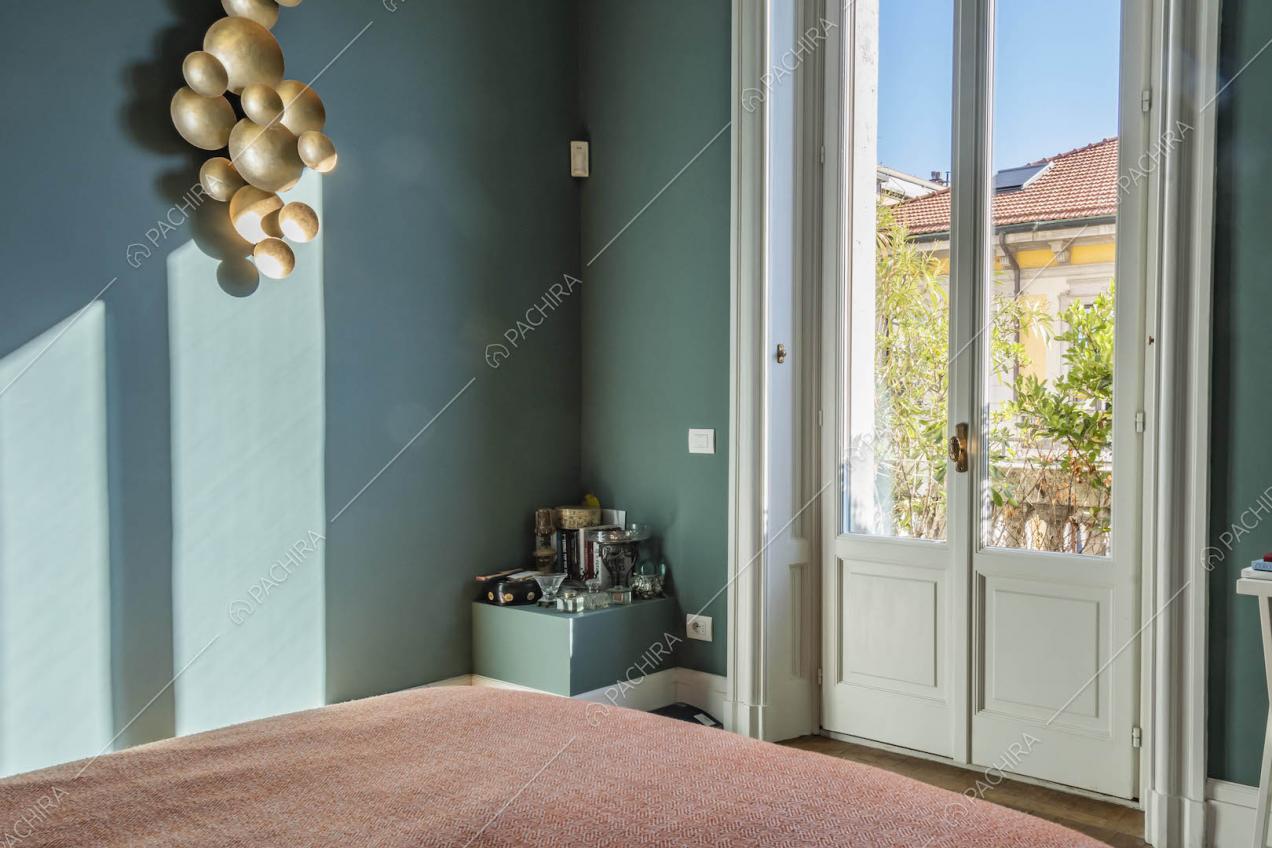 Luminosa camera da letto con porta-finestra con boiserie e pareti blu petrolio