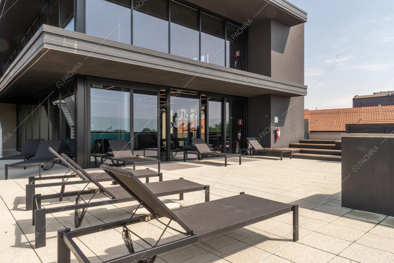 Terrazza con lettini neri, pavimento in piastrelle bianche e vista sulle vetrate dell'attico e superattico