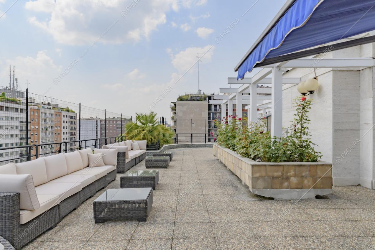 Terrazza con tendone blu, grandi divani bianchi da esterno con tavolini e piante