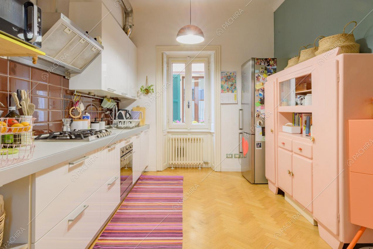 Parete azzurra, credenza rosa e fornelli a gas nella cucina con pavimento in parquet a spina di pesce