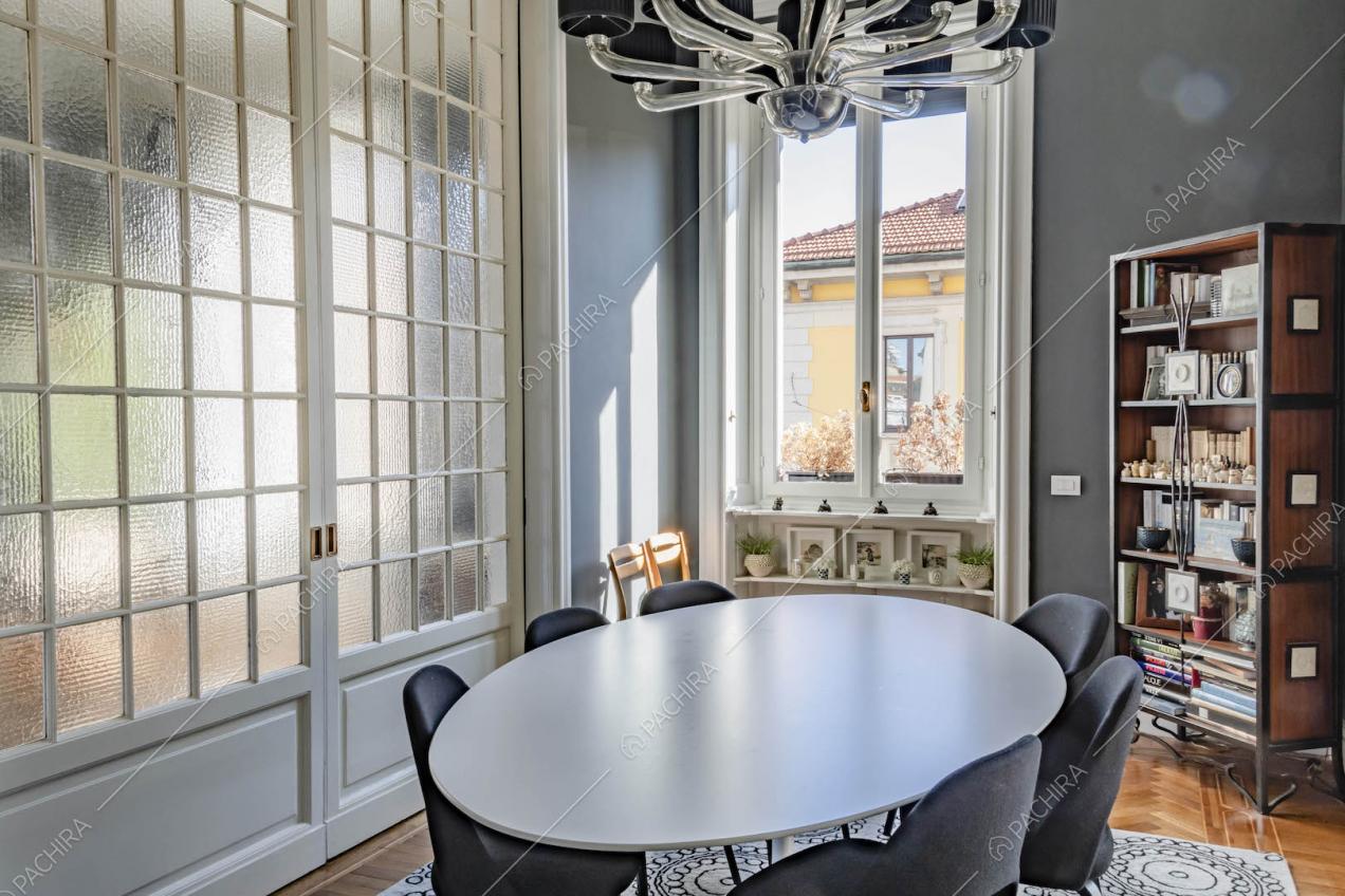 Luminosa sala da pranzo con tavolo bianco, pavimento in parquet a spina di pesce e porte a vetri