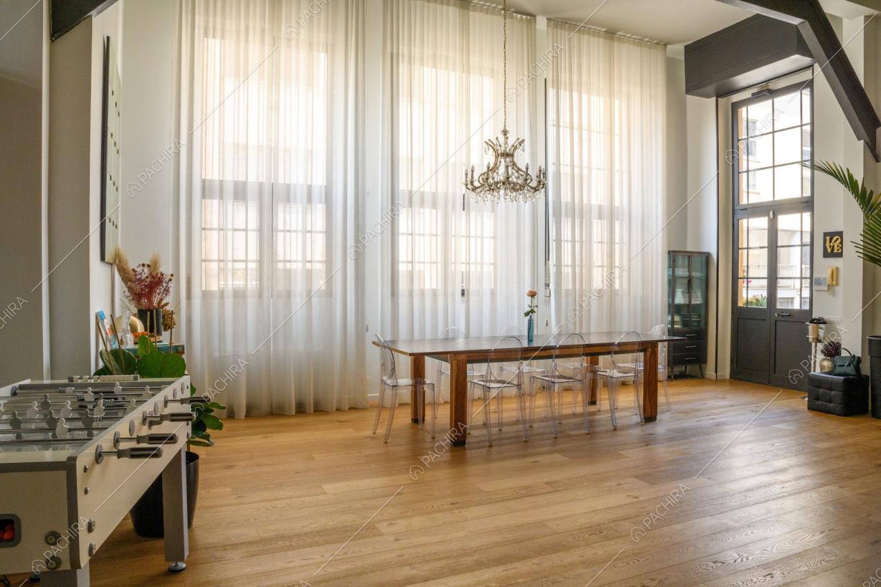 Soggiorno illuminato dalle ampie vetrate in stile industriale con pavimento in parquet e tavolo da pranzo in legno