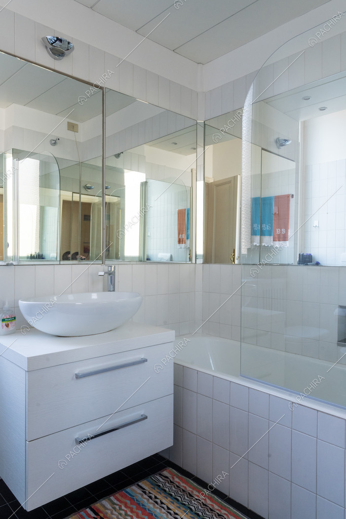 Bagno con soffitto in travi in legno bianco a vista, vasca con piastrelle e specchi