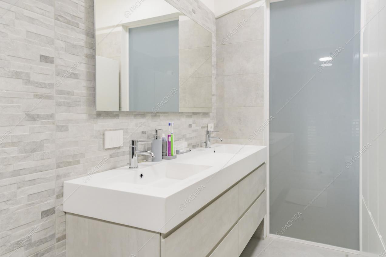 Nel bagno dai toni neutri e dal pavimento in pietra troviamo un doppio lavandino e un ampio specchio