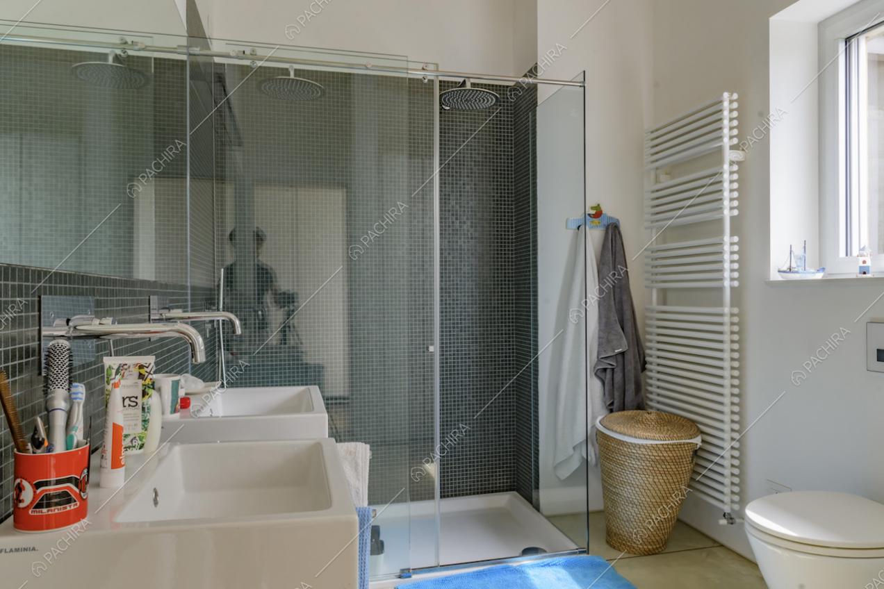 Nel bagno dalle pareti bianche, ampio box doccia con piastrelline blu e doppio lavandino