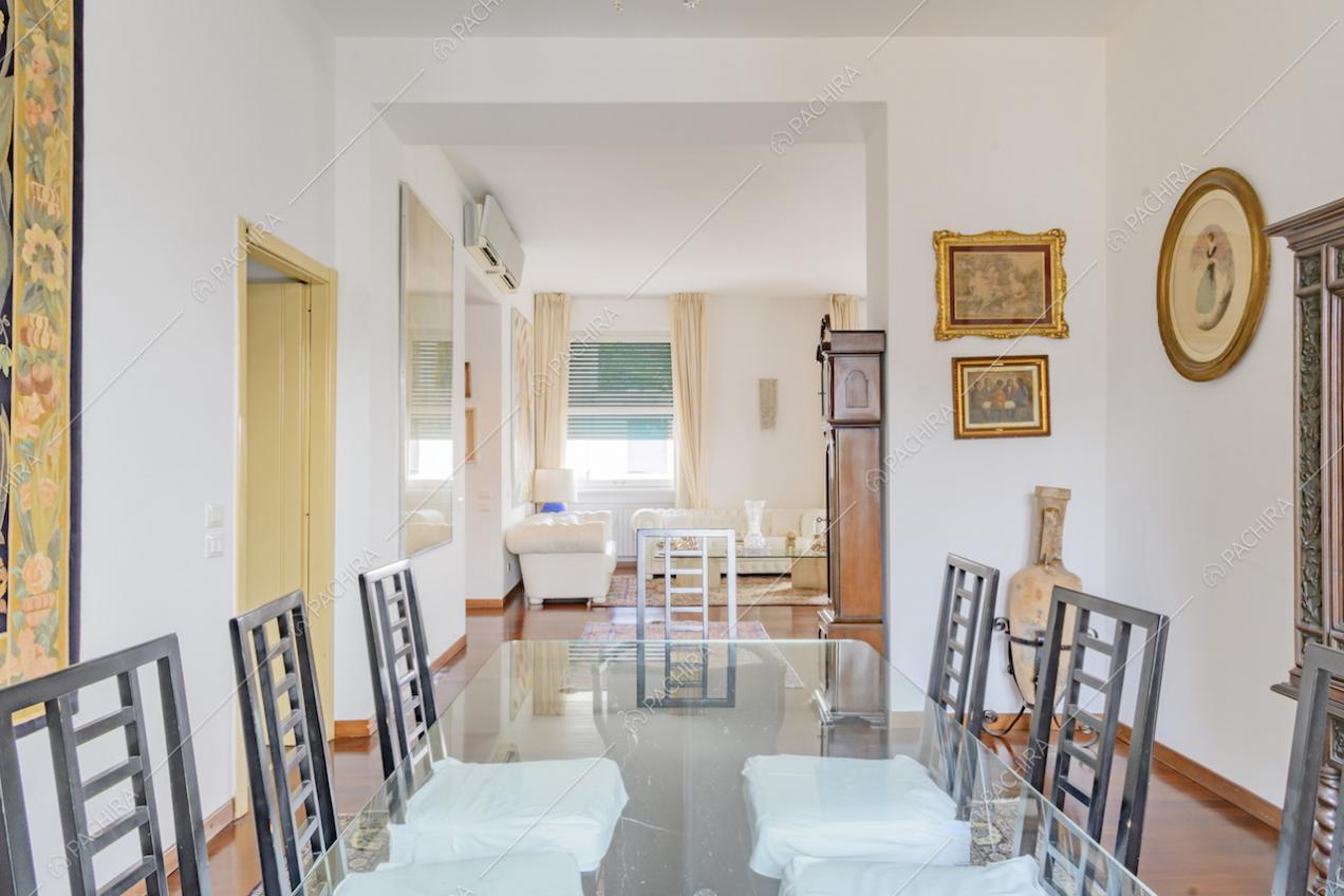 Dal tavolo da pranzo in vetro, con sedie di design, vista sui divani bianchi del soggiorno