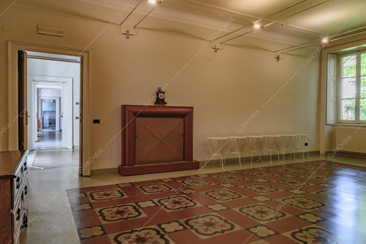 Ampia sala dalle pareti bianche con boiserie sul soffitto, pavimento in marmo e vista sulle altre stanze